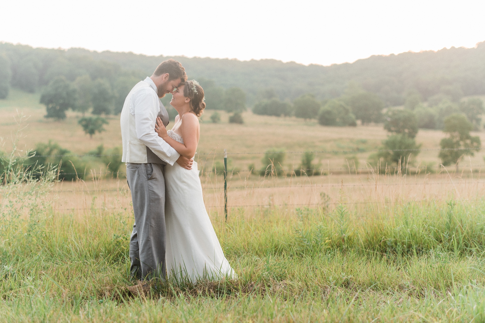 Bride and groom portrait in field at sunset; groom in gray suit, bride in baby's breath flower crown, Little Piney Lodge in Hermann MO