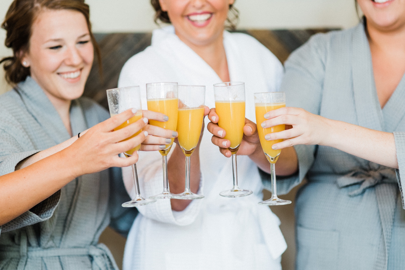 Bride and bridesmaids in monogrammed robes getting ready with mimosas; bridal party; cheers with mimosas