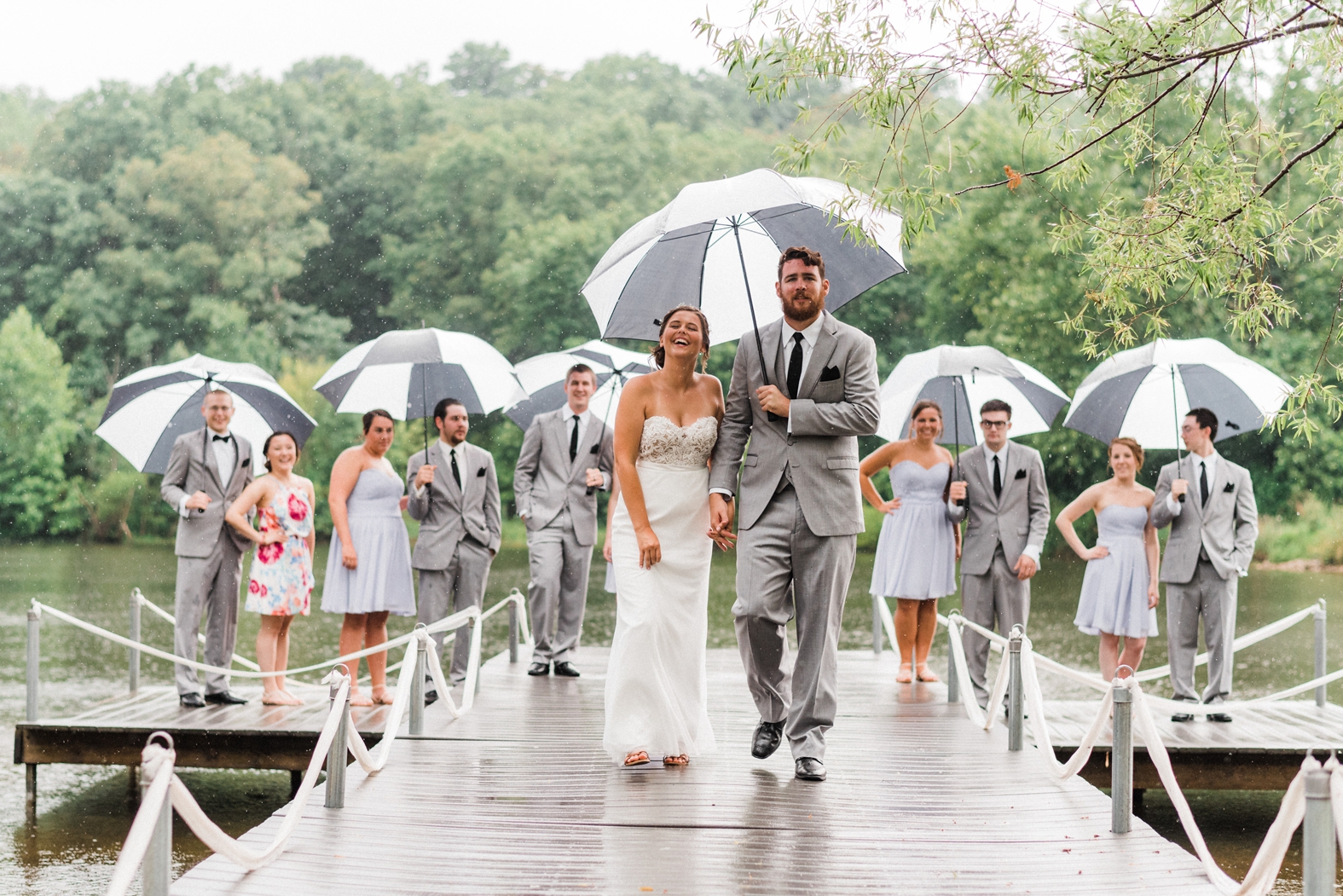 Wedding party on dock in rain with black and white umbrellas.