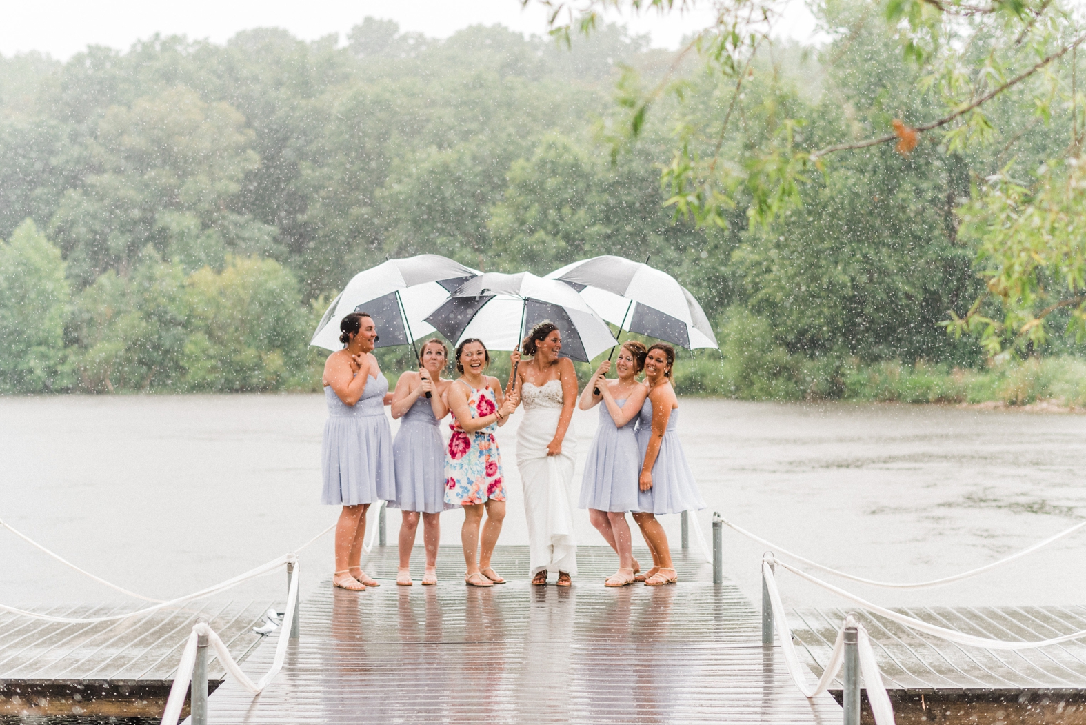 Bride and bridesmaids in rain on dock with black and white umbrellas. Light purple lavender bridesmaids dresses, floral bridesmaid dress.