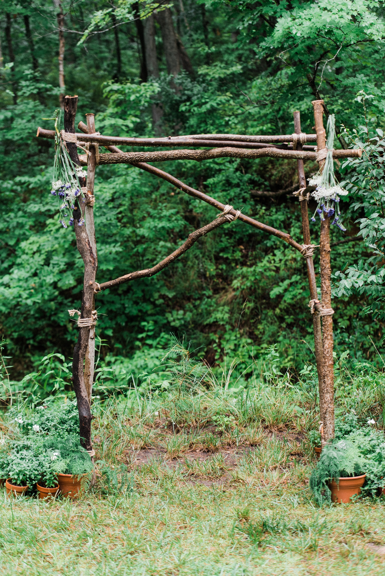Wedding archway trellis for ceremony made of branches with purple flowers and greenery; outdoor wedding ceremony.