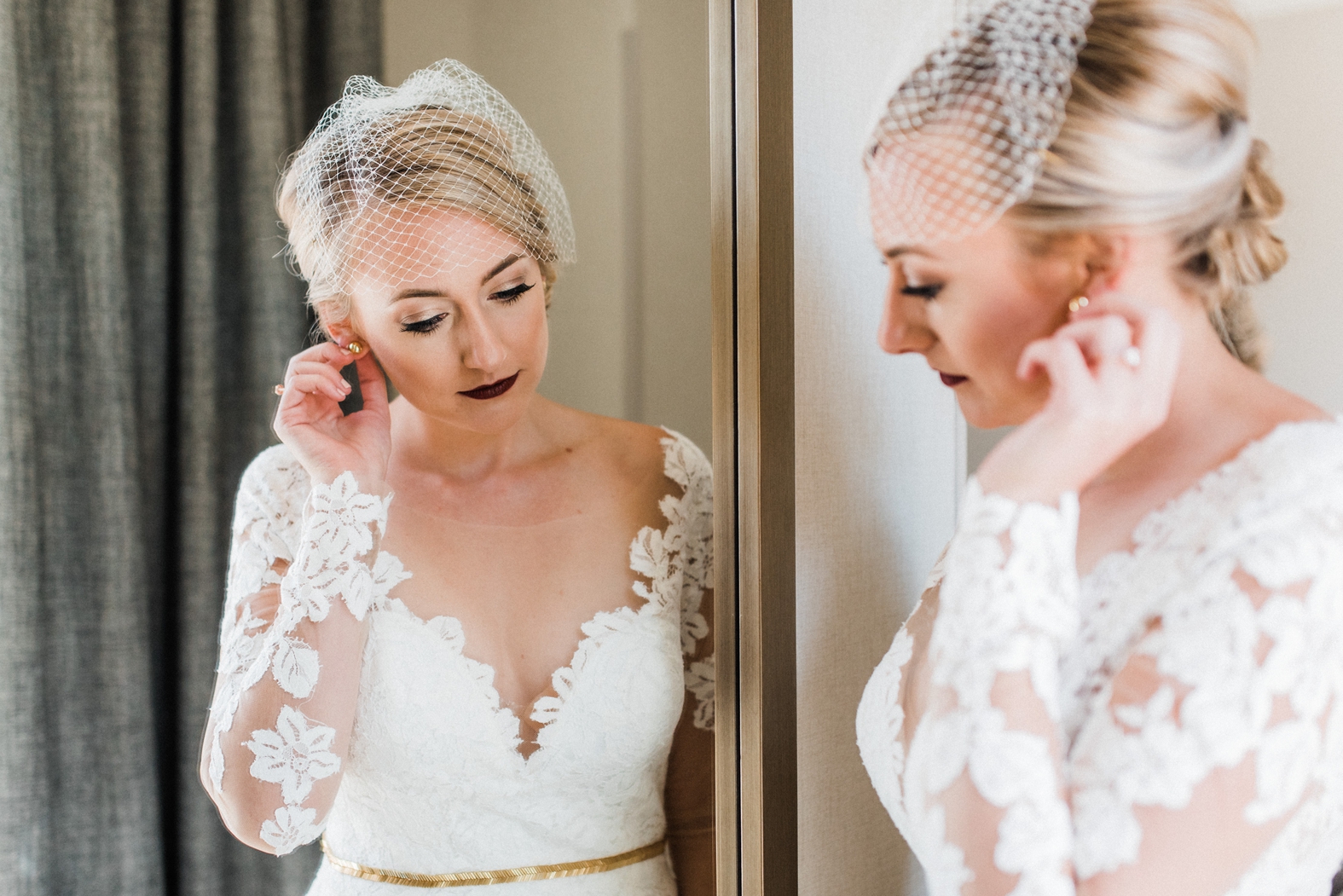 Blonde bride in lace long sleeve wedding dress with gold belt and sweetheart neckline. Birdcage veil and accent lip.