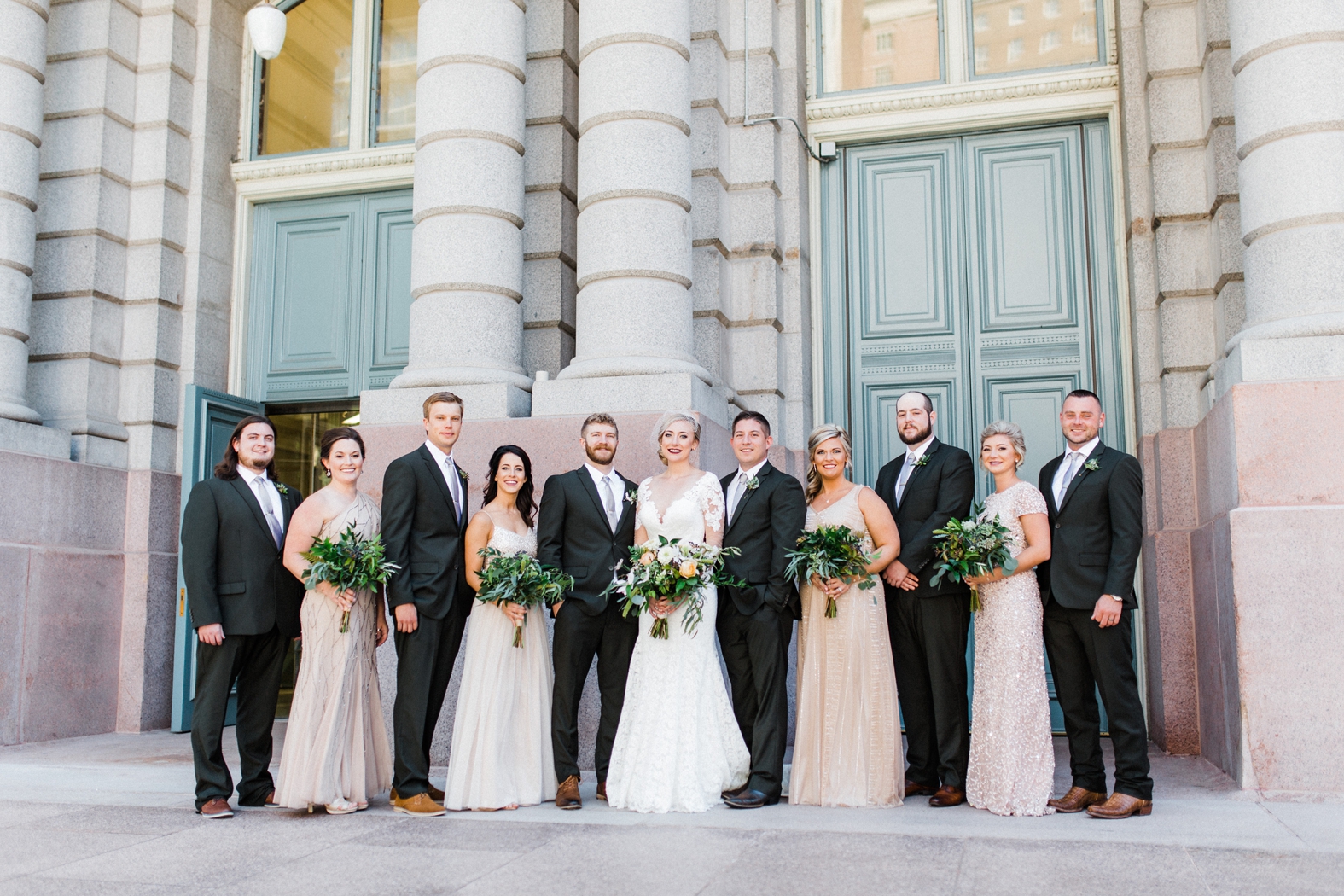 Groomsmen in olive green suits with light gray ties and brown shoes. Bridesmaids in peach, blush, neutral sequined and beaded bridesmaid dresses. Bride in lace long sleeve wedding gown with birdcage veil. Greenery and peach bouquets.
