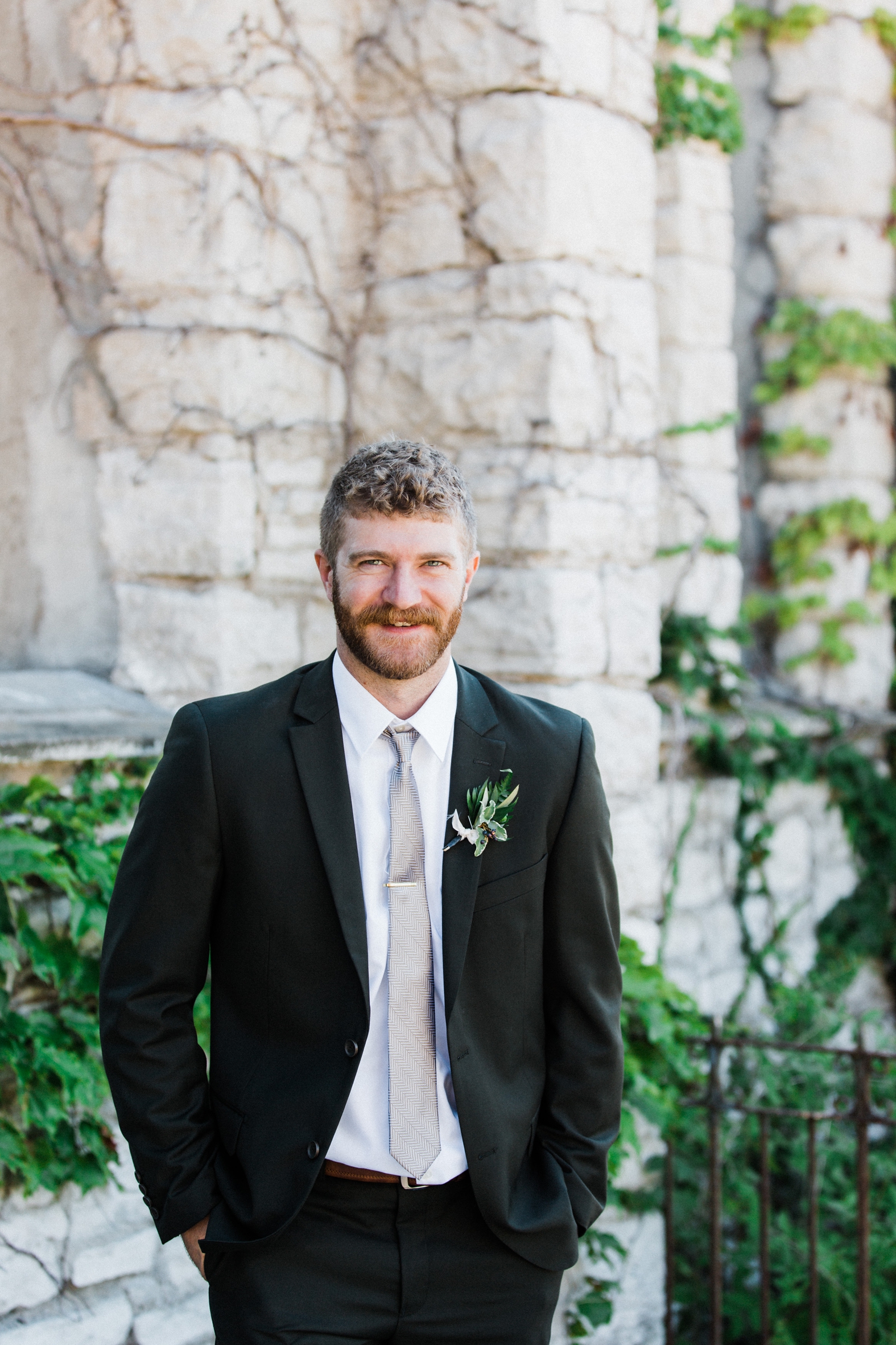 Groom in olive green suit with silver tie and greenery bouquet.