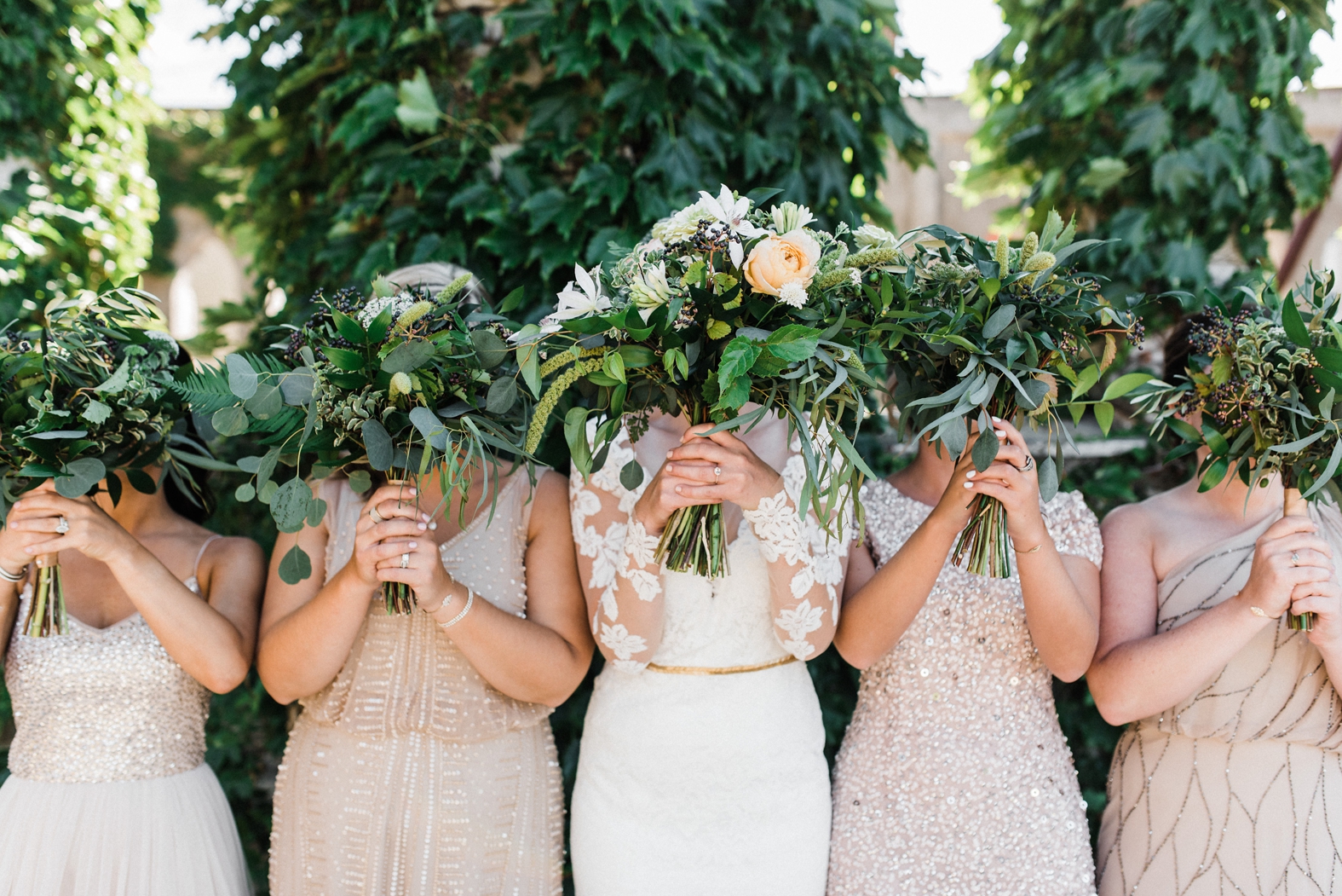 Bridesmaids in blush and neutral sequined and beaded detail bridesmaid dresses. Bride in long sleeve lace wedding gown with gold bridal belt. Bridesmaid bouquets with greenery. 
