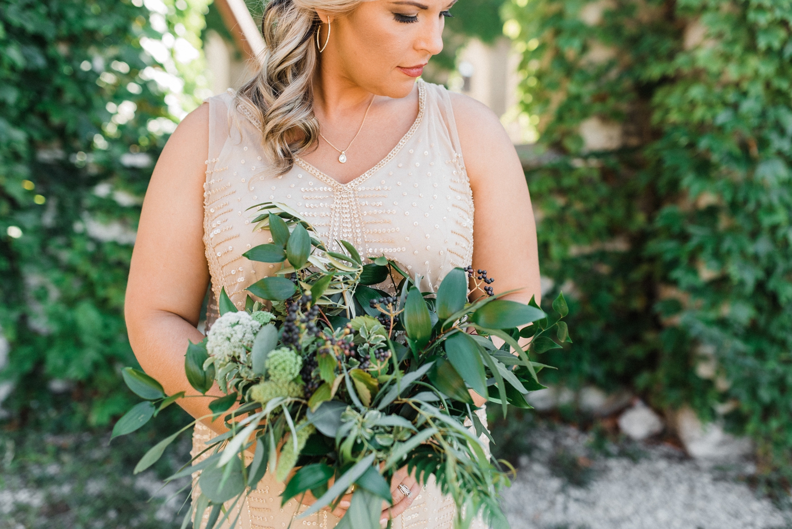 Bride in neutral champagne beaded bridesmaid dress with gold hoop earrings and greenery bridesmaids bouquet.
