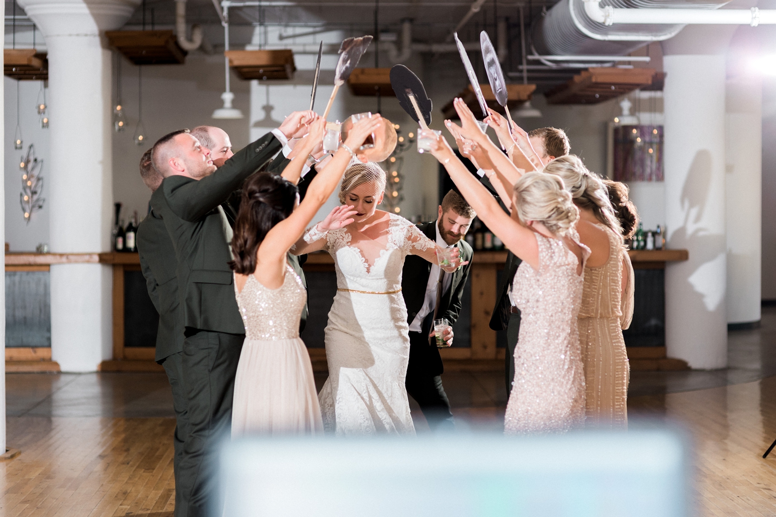 Bride and groom enter on 6th floor of Windows on Washington. Bride in lace long sleeve dress with gold belt and birdcage veil. Groom in olive green suit with silver tie. Bridesmaids in blush and champagne beaded dresses.