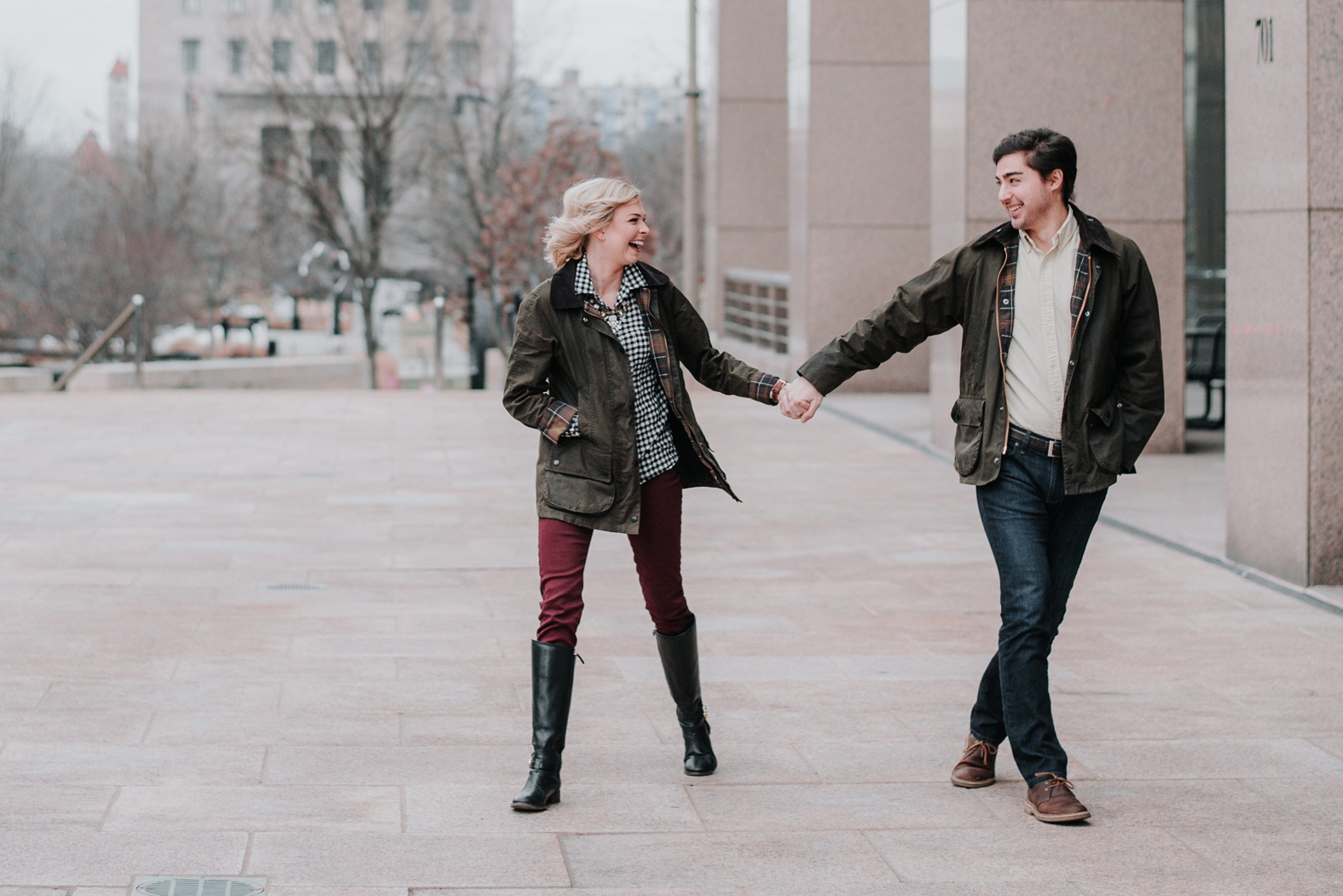 Bride and groom hold hands and laugh at their winter engagement photo session at the Peabody Office Building in St. Louis, MO.