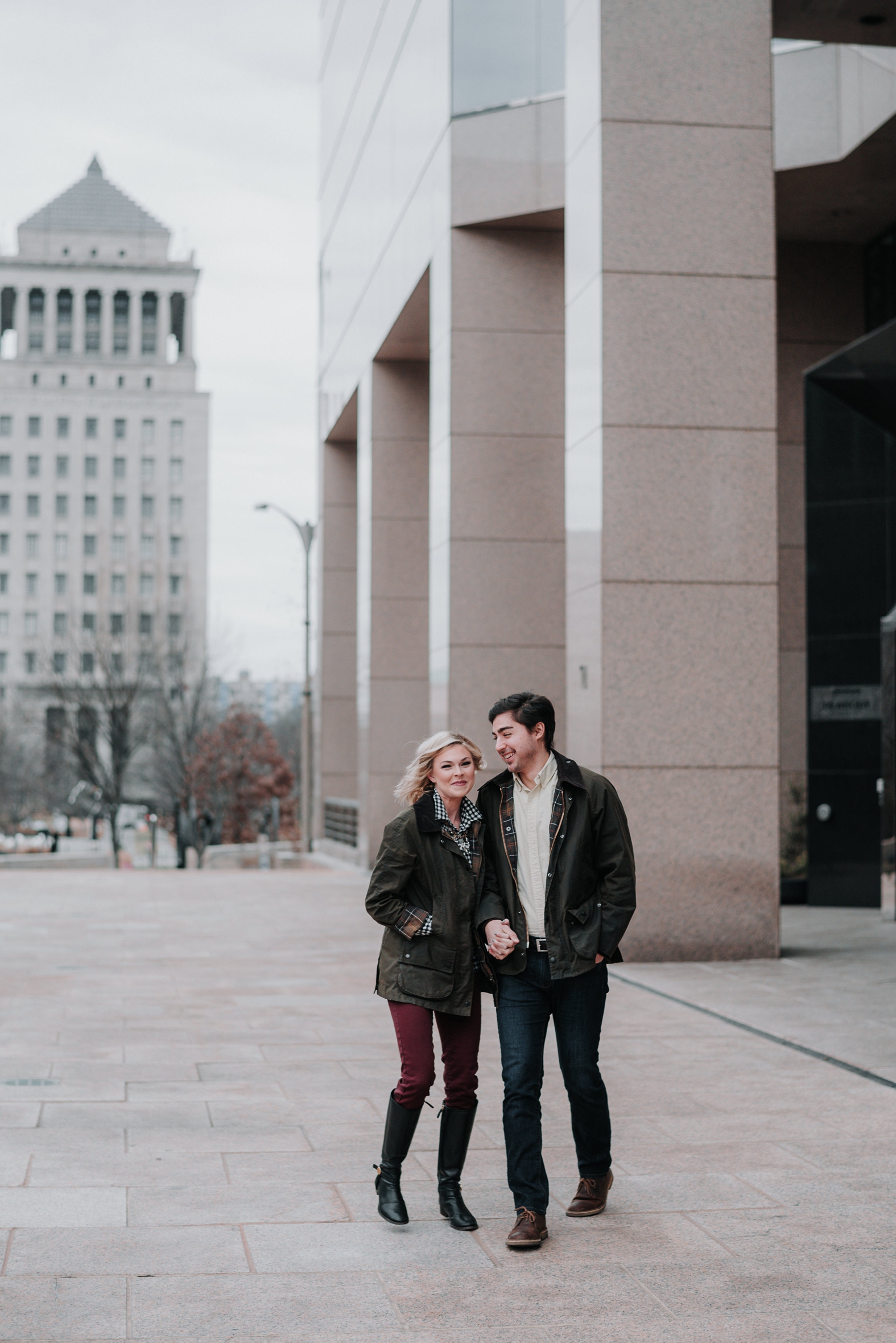 Bride and groom hold hands and laugh during their winter engagement photo session in St. Louis MO in jeans, boots, and plaid shirts.