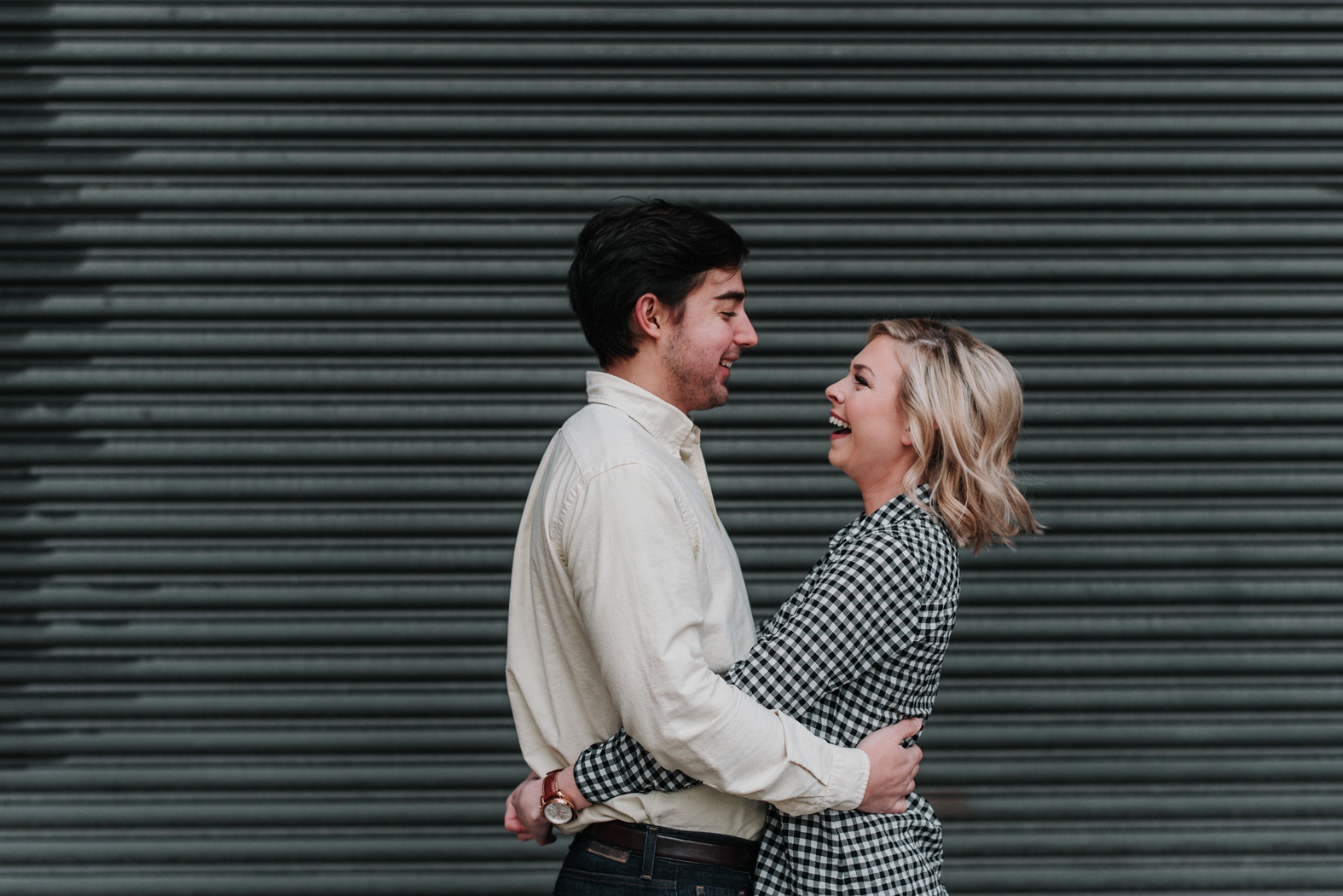 Bride and groom hug each other and laugh during their winter urban downtown St. Louis engagement photo session .