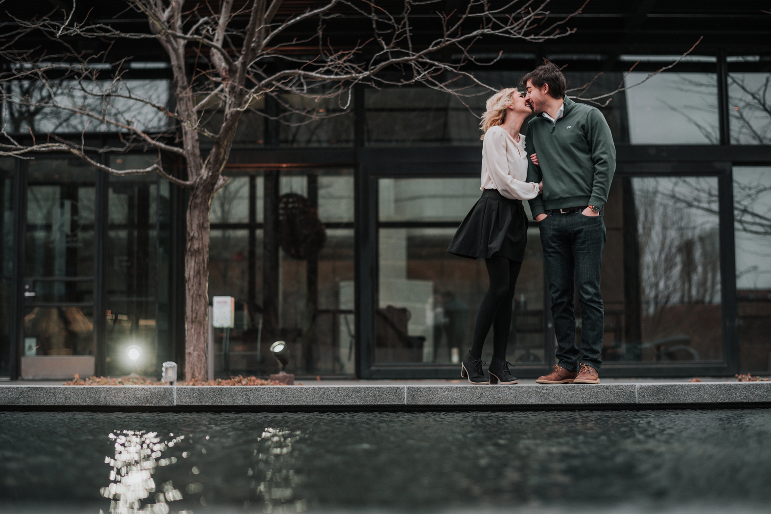 Engaged couple hugs close and kisses on the edge of a fountain in downtown St. Louis during their winter engagement session.