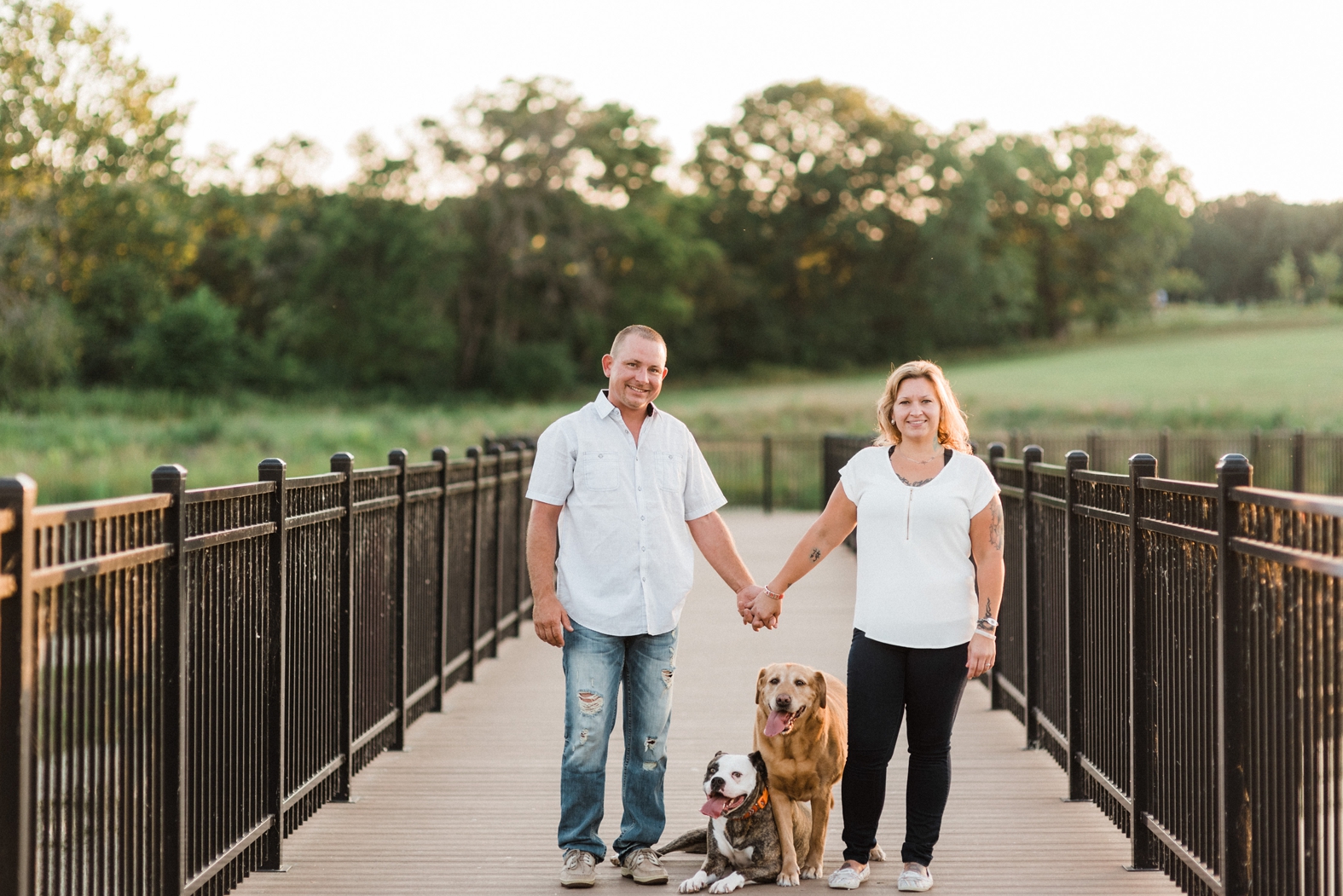 Engaged bride and groom hold hands during their engagement photo session in Broemmelsiek Park in St. Charles, MO with their two dogs.